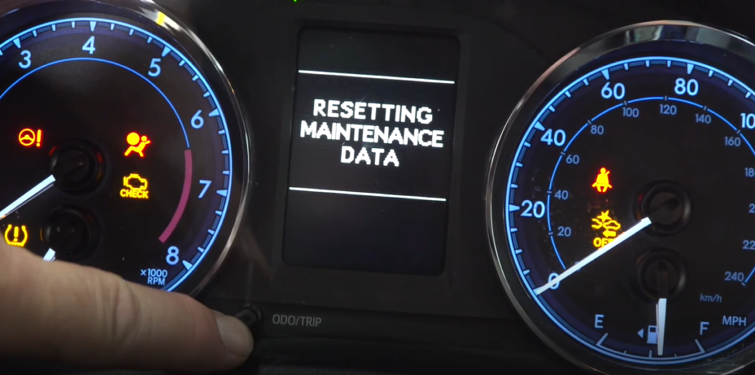 Car interior with mileage, RPM, and fuel level gauges, and text 'Resetting maintenance data' in the center