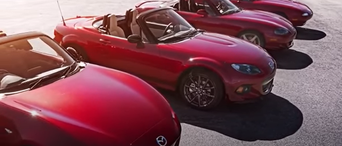 Red Miatas lined up, including older models